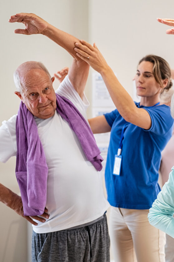 Senior man participating in a stretching exercise with staff.