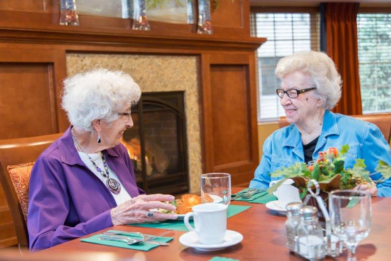 Two smiling residents enjoying tea in a dining room