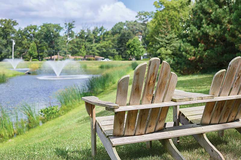 Adirondack chairs by a serene pond with fountains