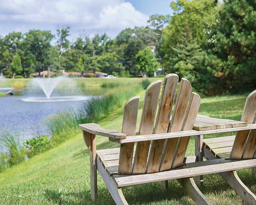 Adirondack chairs by a serene pond with fountain
