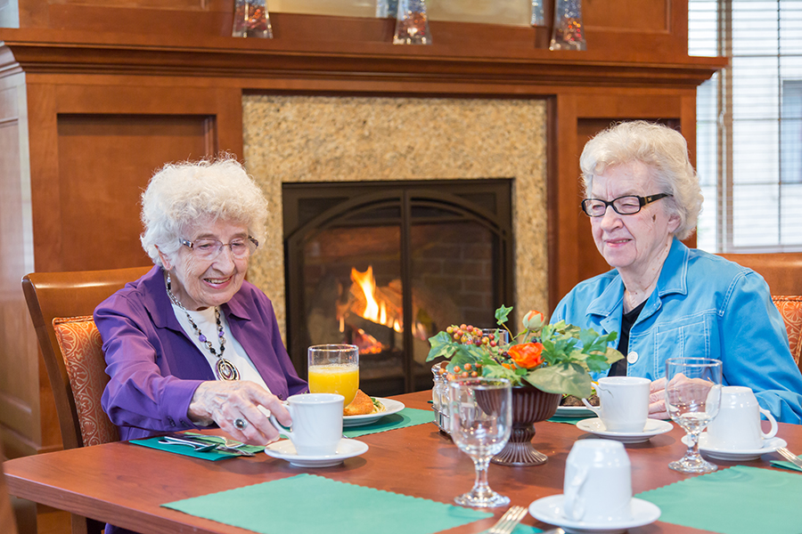 Two elderly women enjoying breakfast near a fireplace