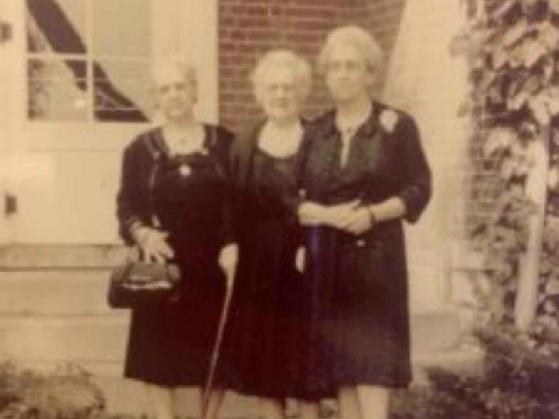Three women in dresses standing outside a building