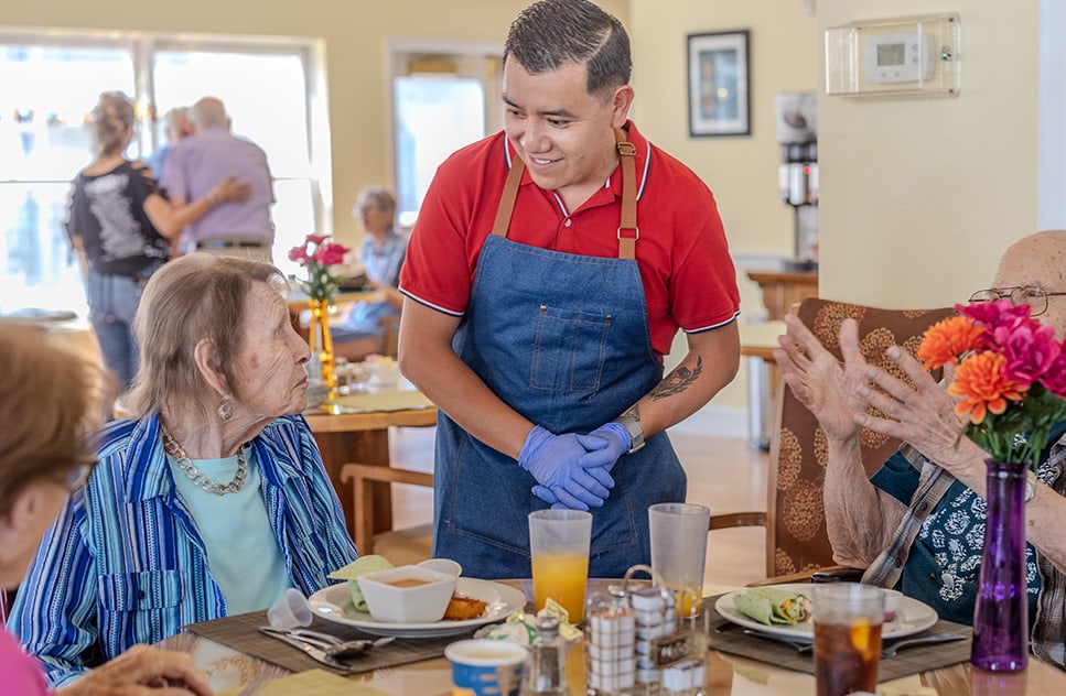 Residents enjoying a meal with staff assistance in the dining room