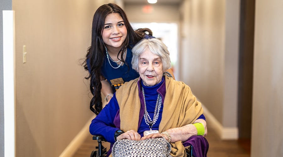 Resident in a wheelchair with a staff member in a hall