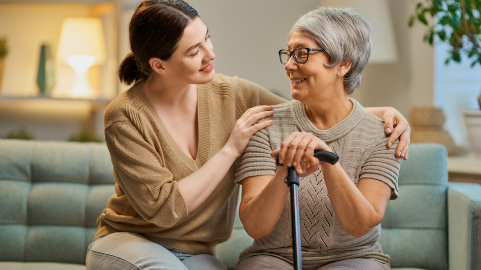 Caregiver assisting an elderly woman on a couch