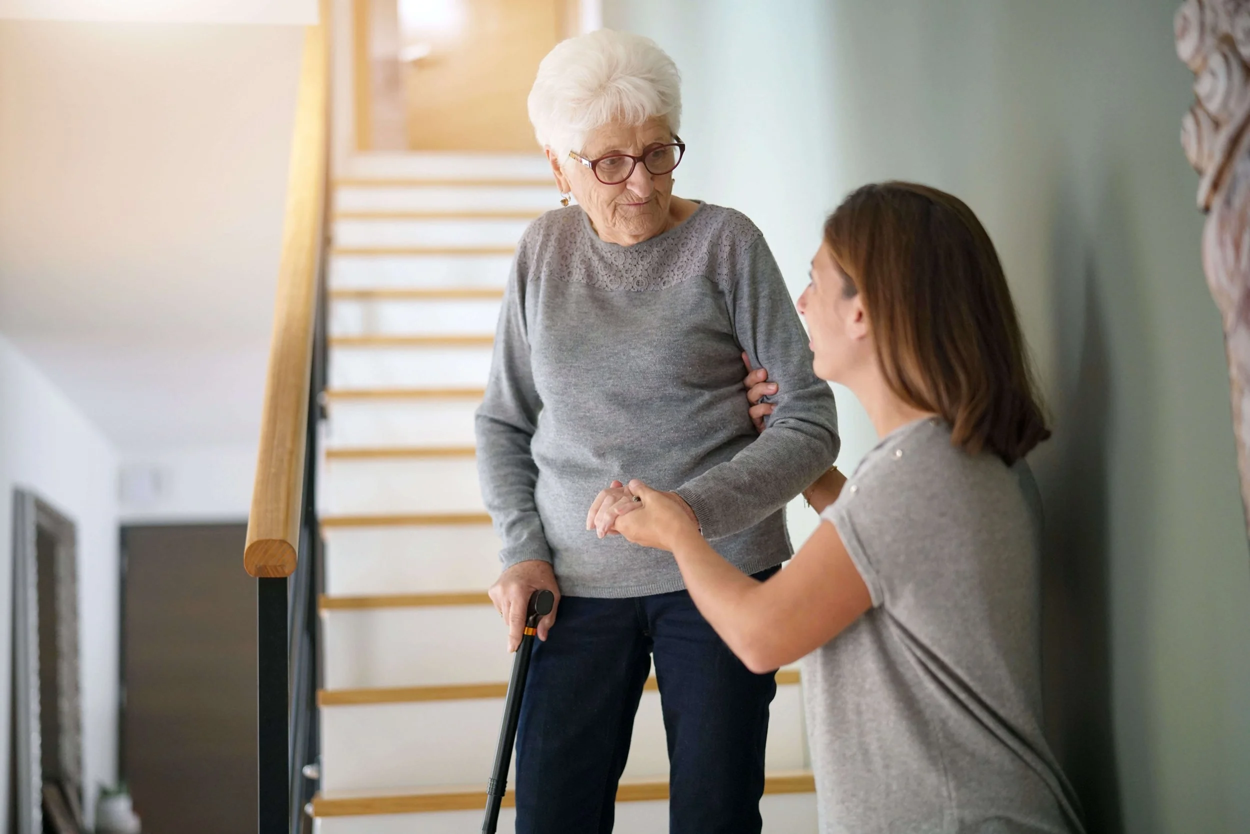 Elderly woman assisted on stairs by caregiver.