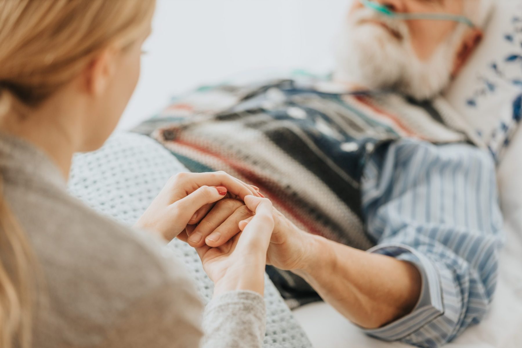 Caregiver gently holding a patient's hand.
