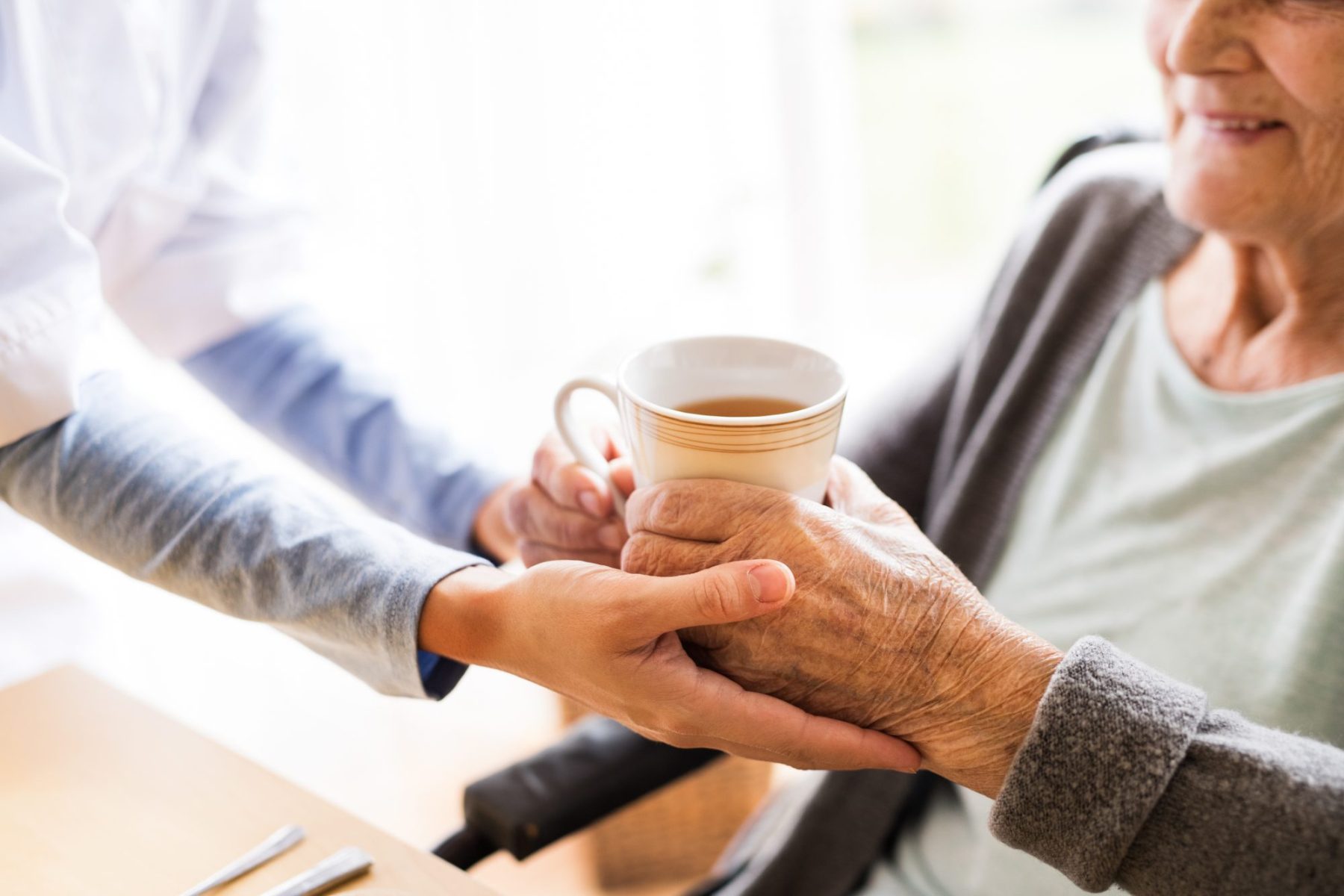 Caregiver handing a warm beverage to a senior.