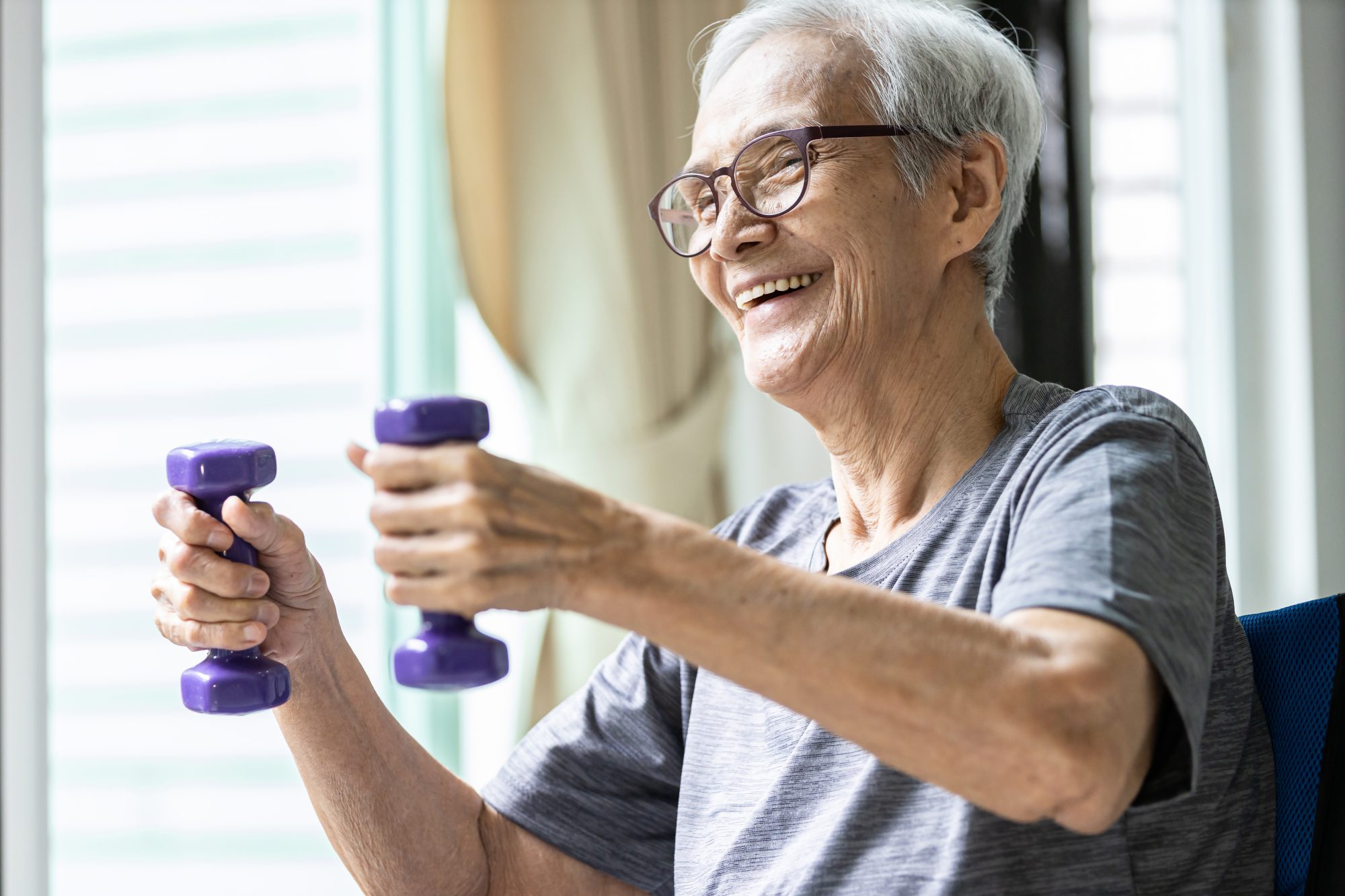 Senior man exercising with dumbbells indoors.