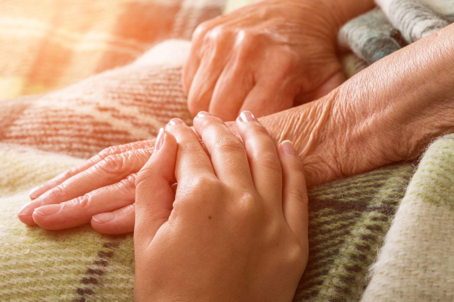 Hands of a caregiver and a senior person resting together.