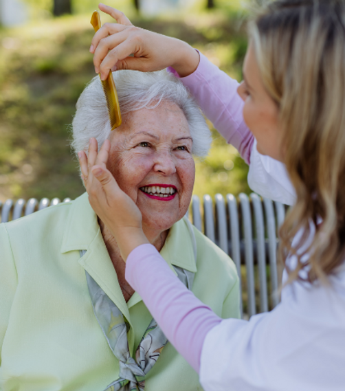 Woman styling hair of senior outdoors.
