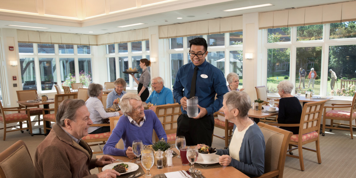 Dining room scene with residents and staff serving food.