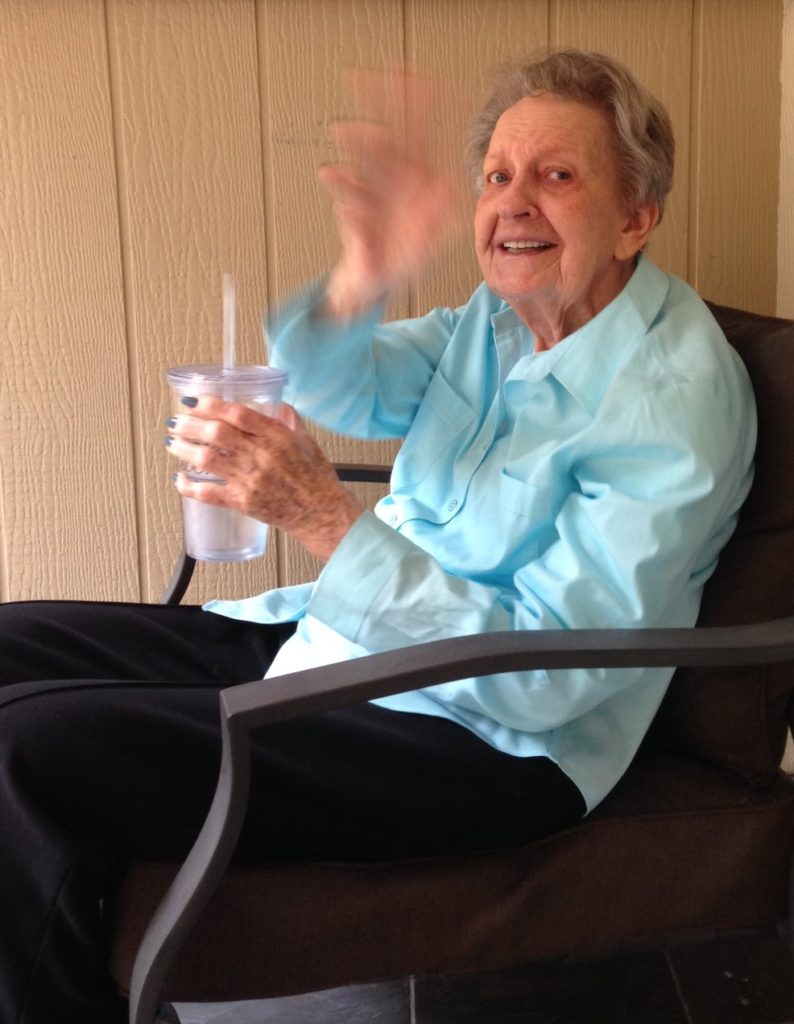 An elderly woman waving while seated.