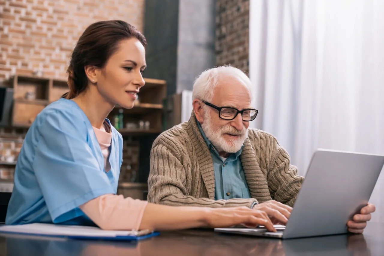 Healthcare worker assisting an elderly man with a laptop.