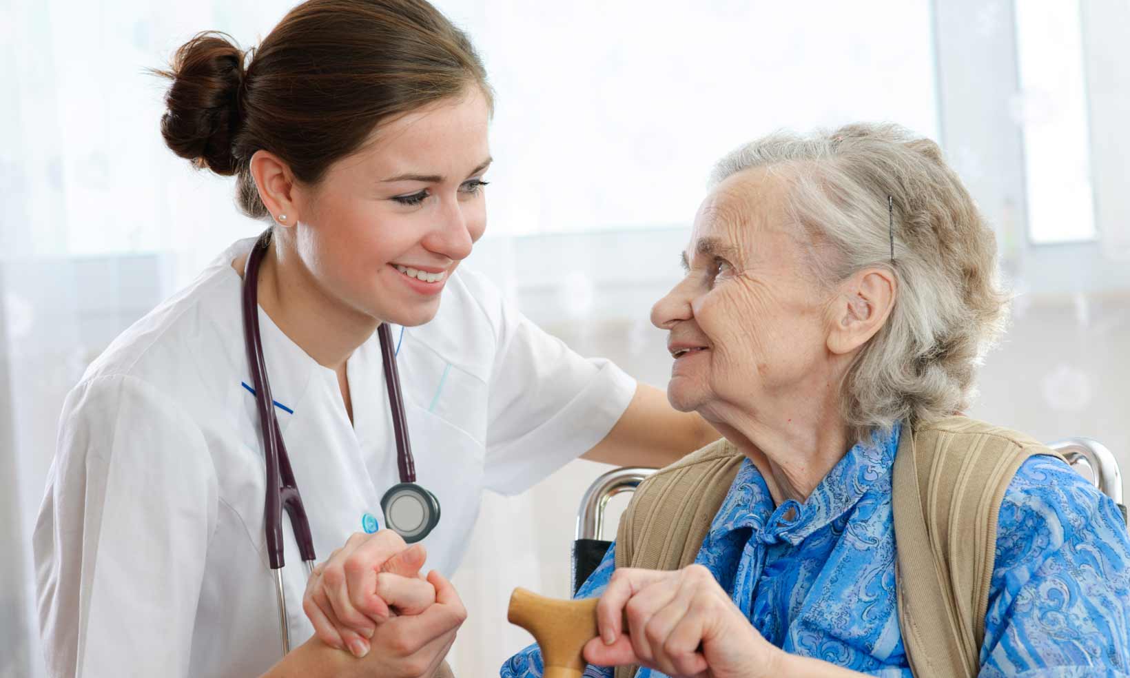 Caregiver interacts with elderly resident indoors.