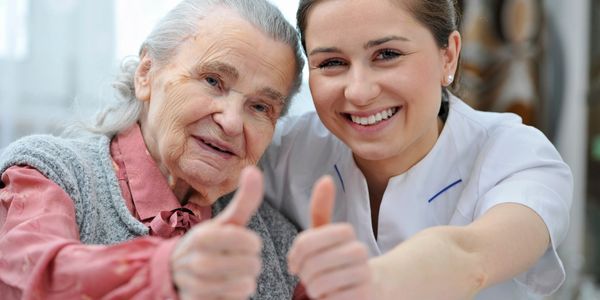 Senior resident and caregiver smiling with thumbs up