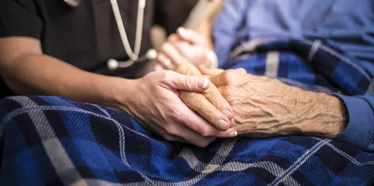 A caregiver holds an elderly person's hand.