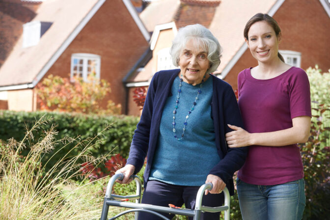 Elderly woman with a walker and caregiver in garden