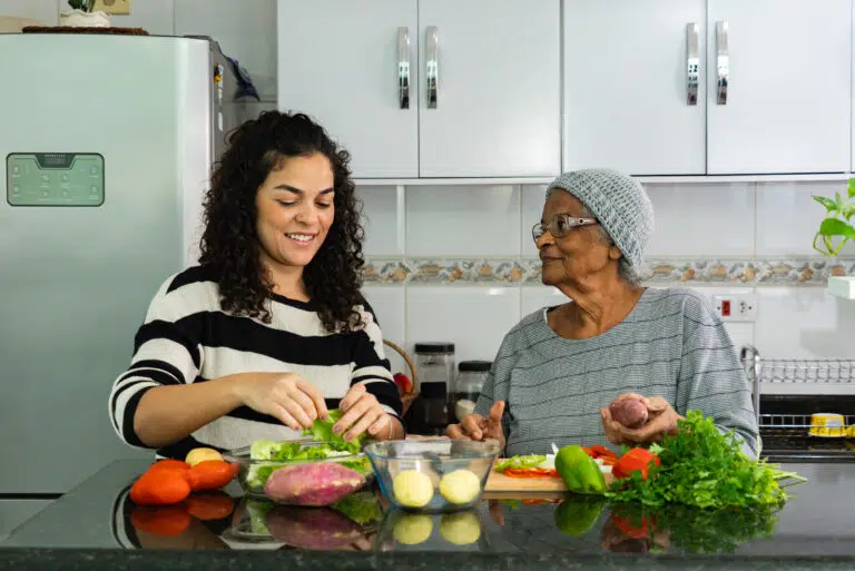 Woman cooking with elderly resident in a kitchen.