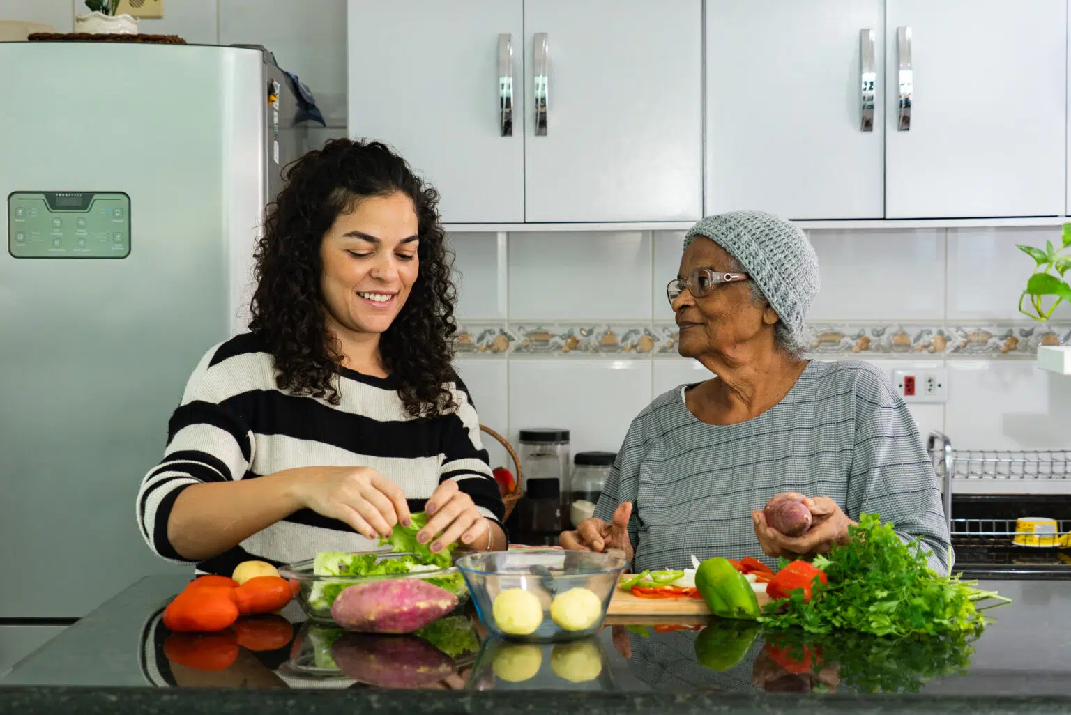 Senior woman cooking with a caregiver in the kitchen.