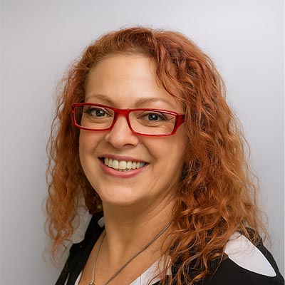 Woman with curly red hair and glasses smiling.