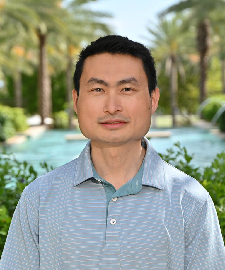 Man standing outdoors near a pool area with palm trees.