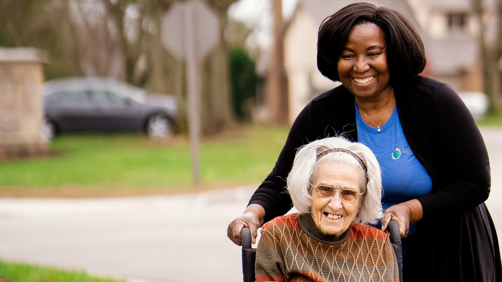 Caregiver assisting a smiling elderly woman outdoors.