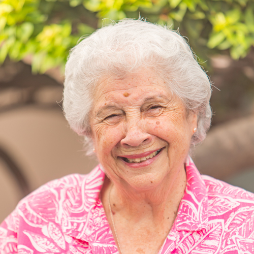 Senior woman smiling outdoors with greenery in the background