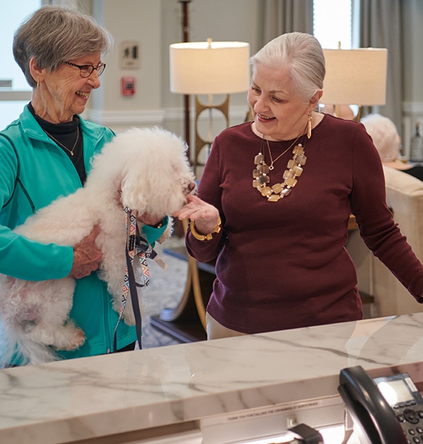 Two women interacting with a small dog in a common area