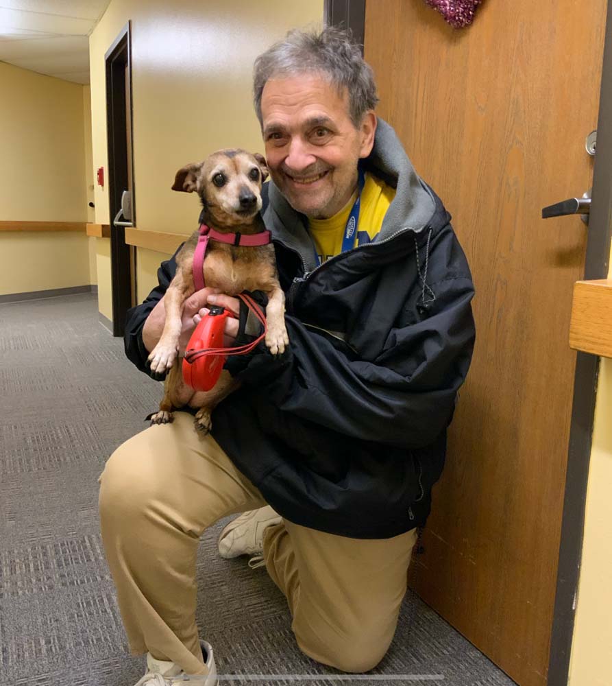 A resident kneeling with a small dog in a hallway