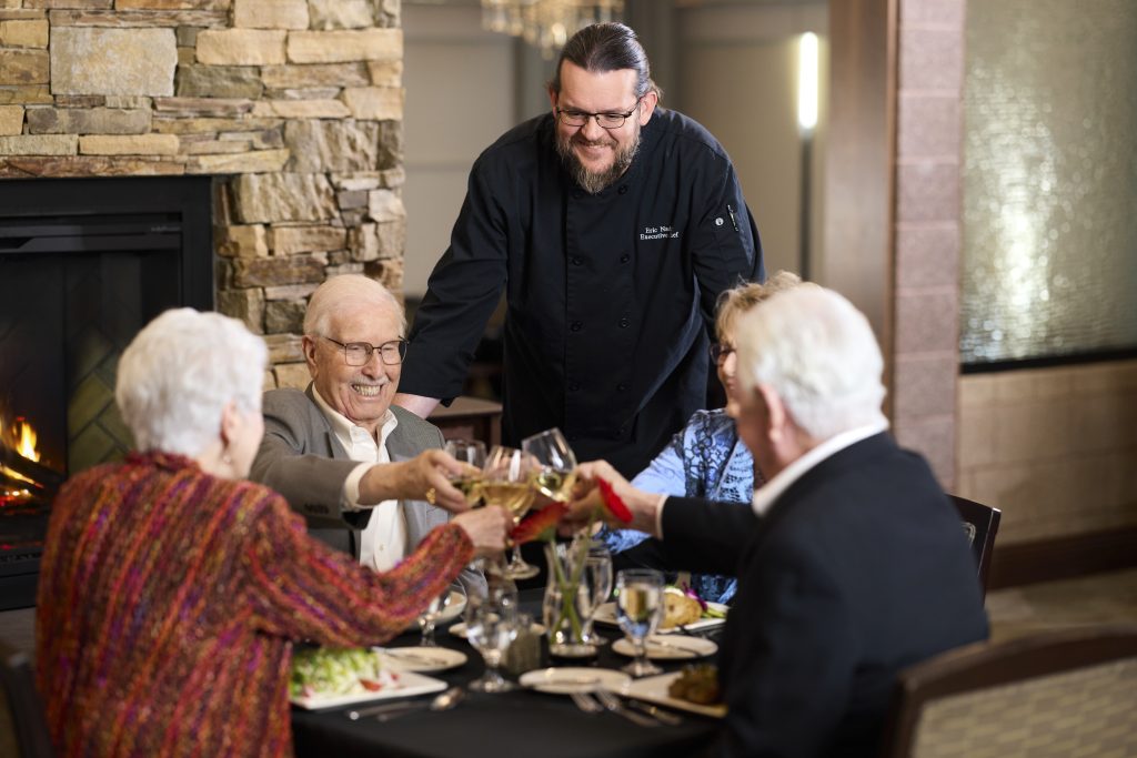 Residents enjoying a meal with a chef at a dining table
