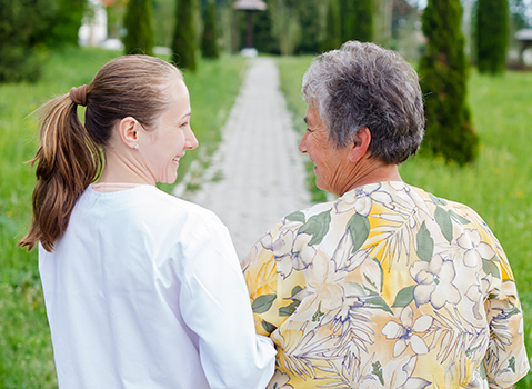 A caregiver and senior resident walking outdoors in a garden