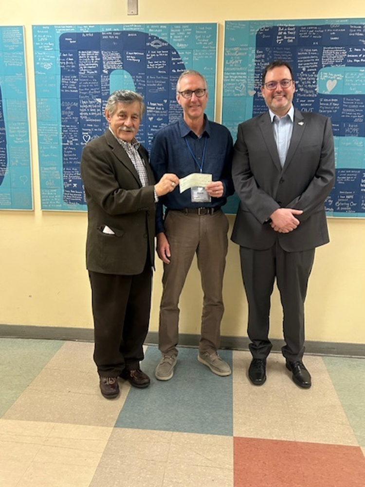Three men in a facility corridor holding a check