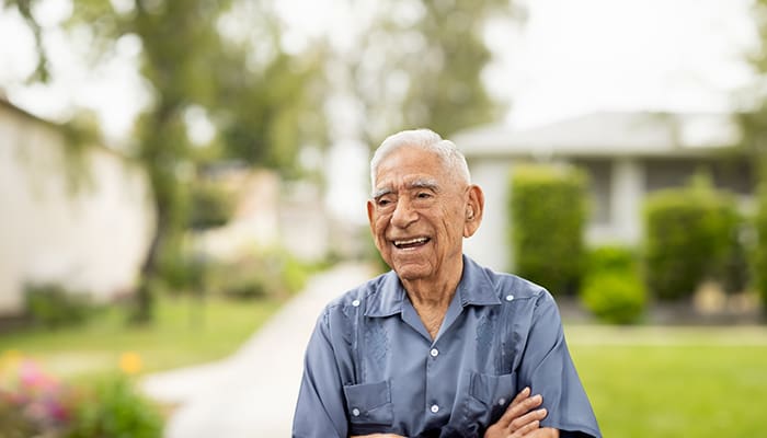 A smiling elderly man standing outdoors in a garden setting