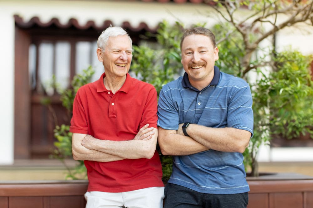 Two men smiling and standing outside in a garden area