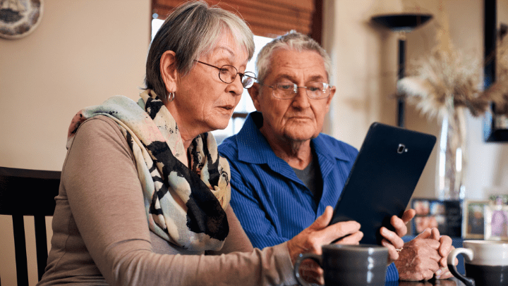 Two seniors using a tablet at a dining table