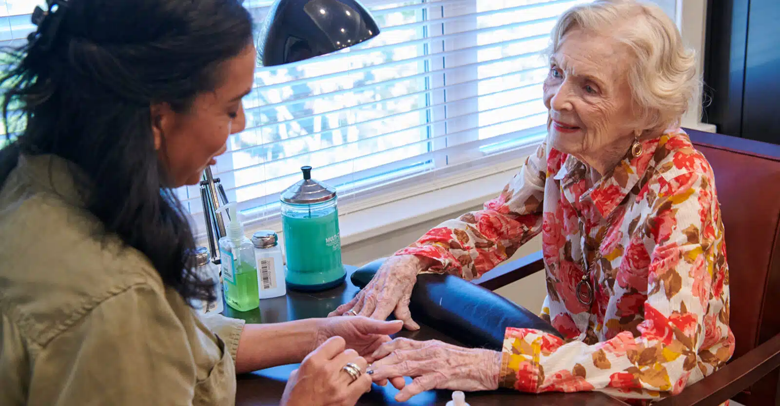 A caregiver providing a manicure to a resident in a cozy setting.