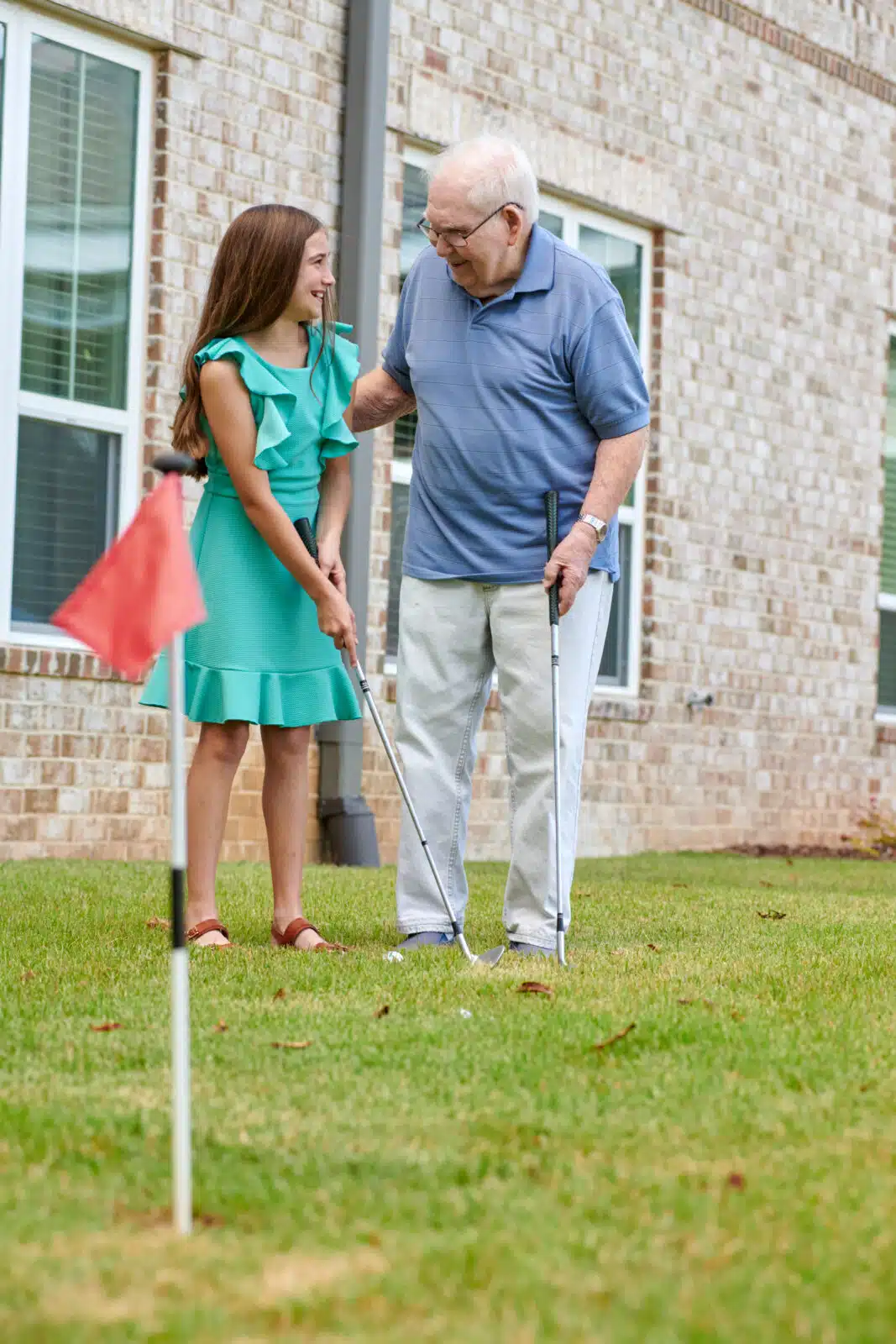 An older man playing golf with a young girl outdoors