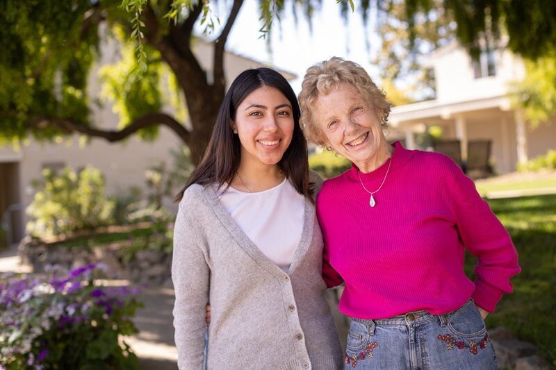A staff member and resident smiling outdoors