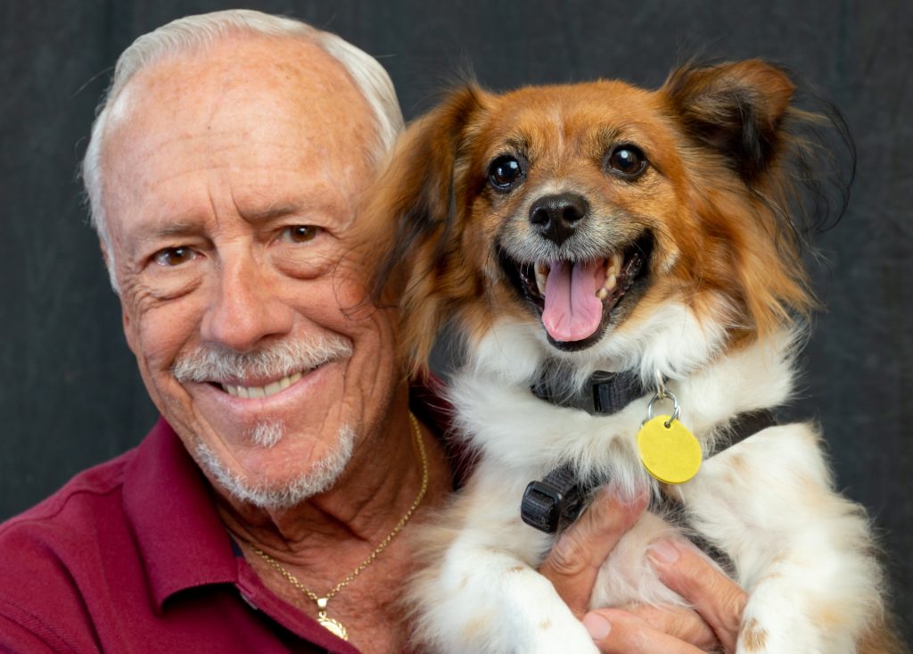 A senior man smiling while holding a dog