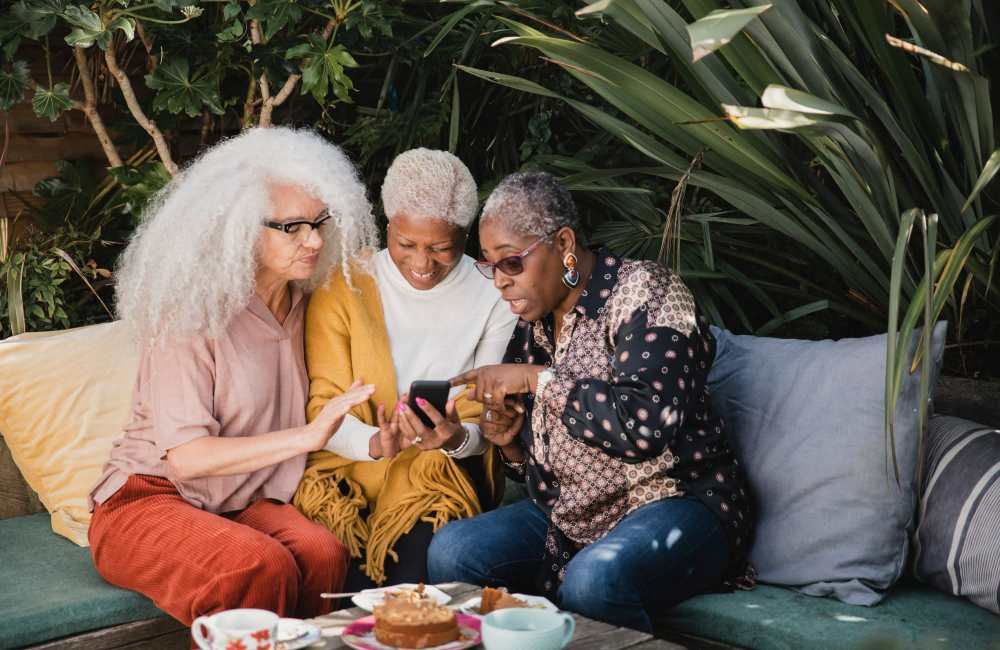 Three women enjoying cake and a smartphone outdoors