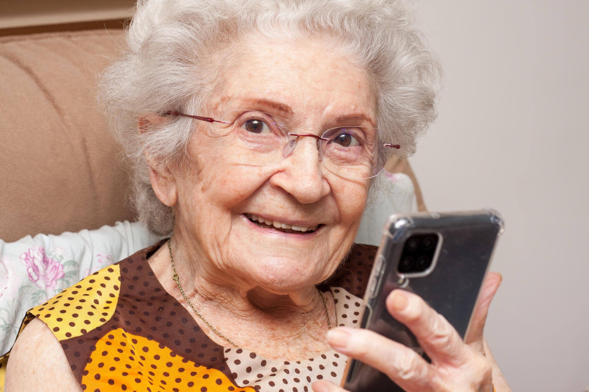 An elderly woman smiling while holding a smartphone
