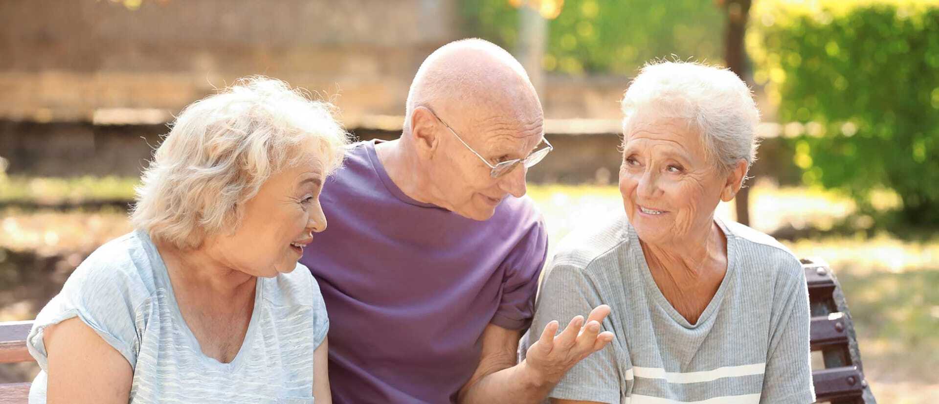 Three seniors sitting on a bench outdoors, smiling and conversing