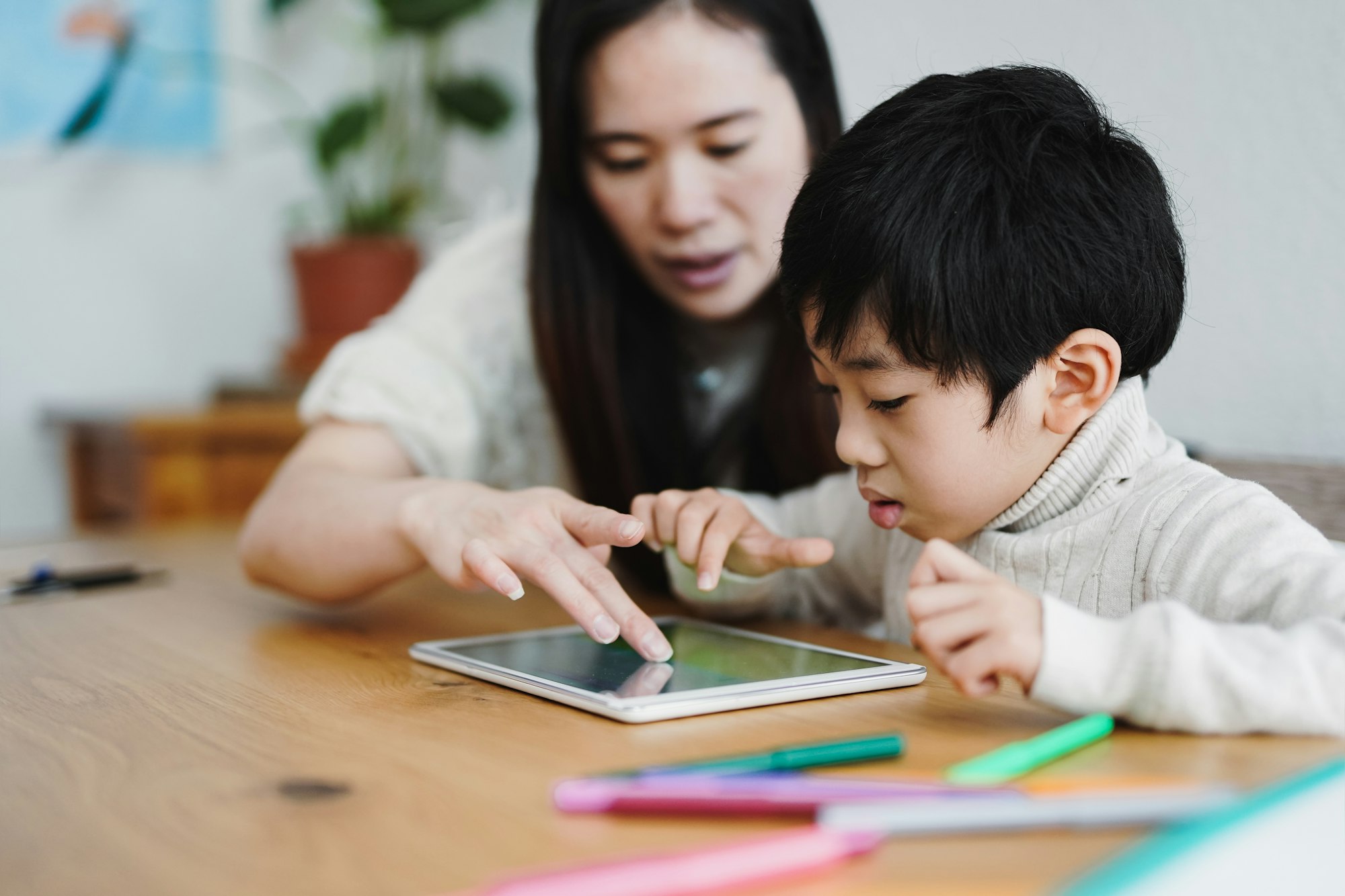 Adult assisting a child with a tablet at a table