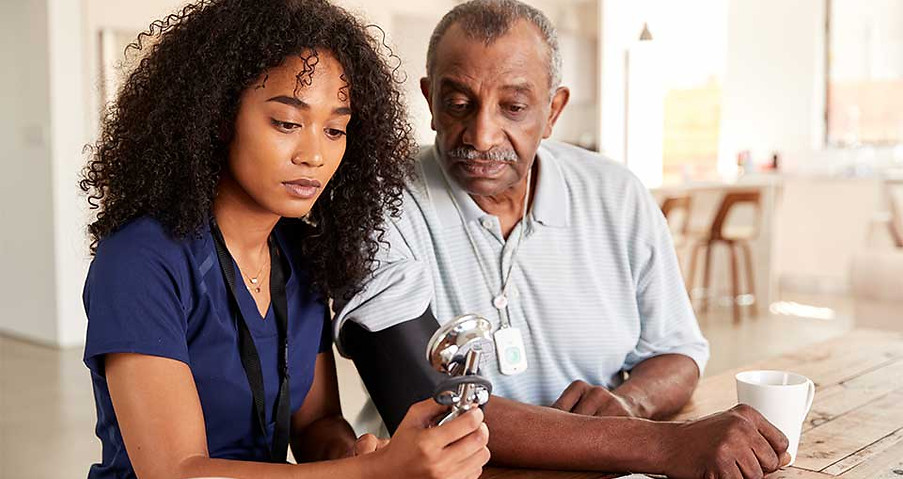 A caregiver assisting a senior man check his blood pressure.