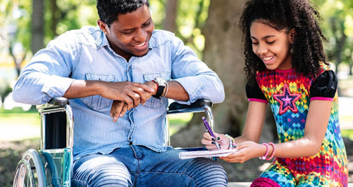 A man in a wheelchair and a girl drawing outdoors.