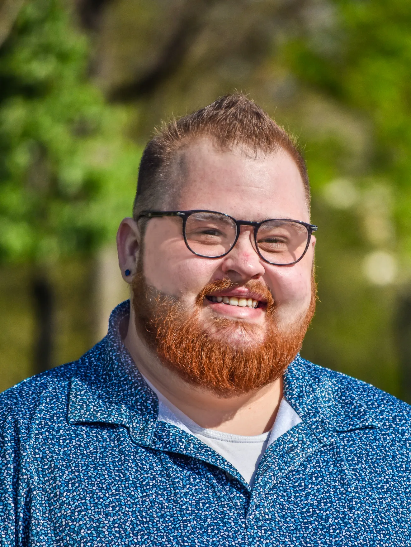 Smiling resident outdoors with greenery in background.
