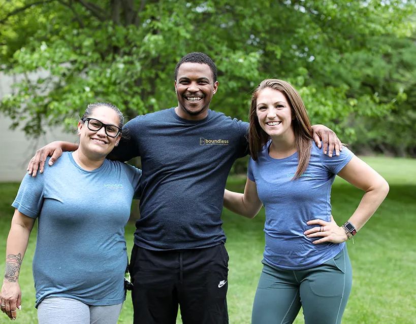 Three staff members posing outdoors in a green setting.