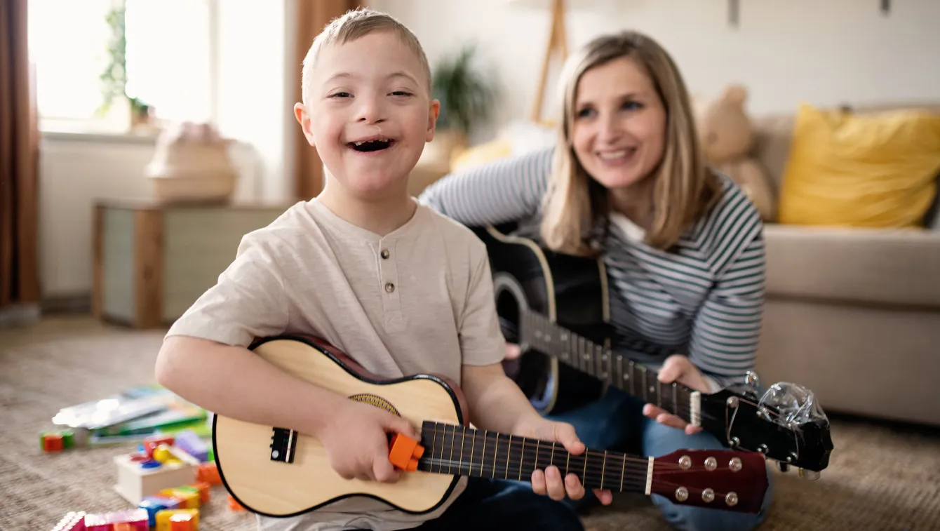 Child playing ukulele with adult in a cozy living area.