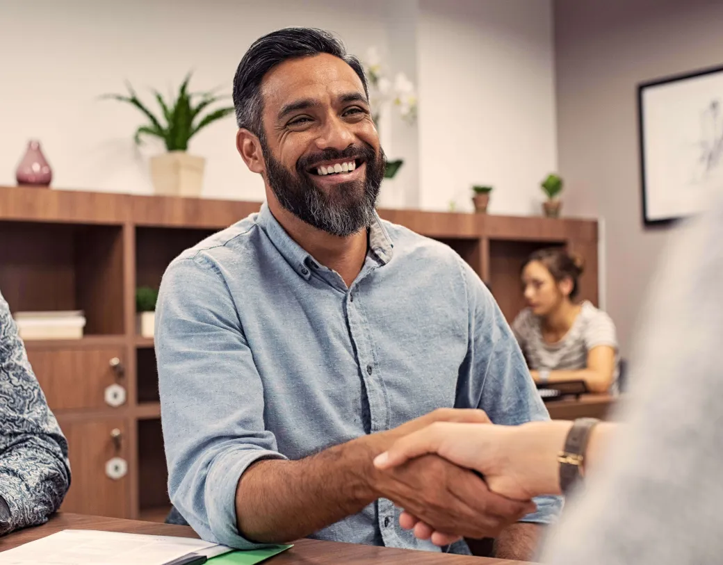 Man smiling and shaking hands in an indoor setting.